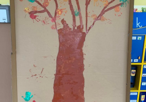 Plastykoterapia w grupie 1. Zdjęcie przedstawia namalowane, jesienne drzewo. Kolorowe liście to odciśnięte dłonie dzieci.